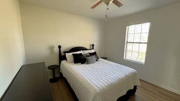 Une chambre à coucher avec un lit, un ventilateur de plafond, une fenêtre et une petite table.