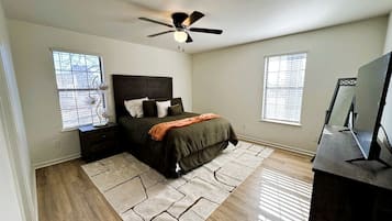 A bedroom with a bed, nightstands, a ceiling fan, a TV, and a window with blinds.