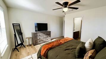 A bedroom with a bed, a ceiling fan, a TV, a dresser, and a mirror.