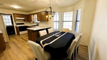 A dining area with a table set for four, a kitchen with wooden cabinets, and a ceiling light fixture.