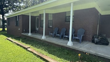 A building with a covered porch, brick walls, and several plastic chairs.