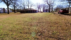 A residential area with houses, a grassy yard, and a red vehicle parked on the right. - Peaceful Retreat with Expansive Yards & Cozy Outdoor Spaces in Alexander, Arkansas (Alexander)