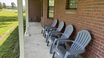 A covered outdoor seating area with rows of chairs against a brick wall, a concrete floor, and a grassy field in the background.