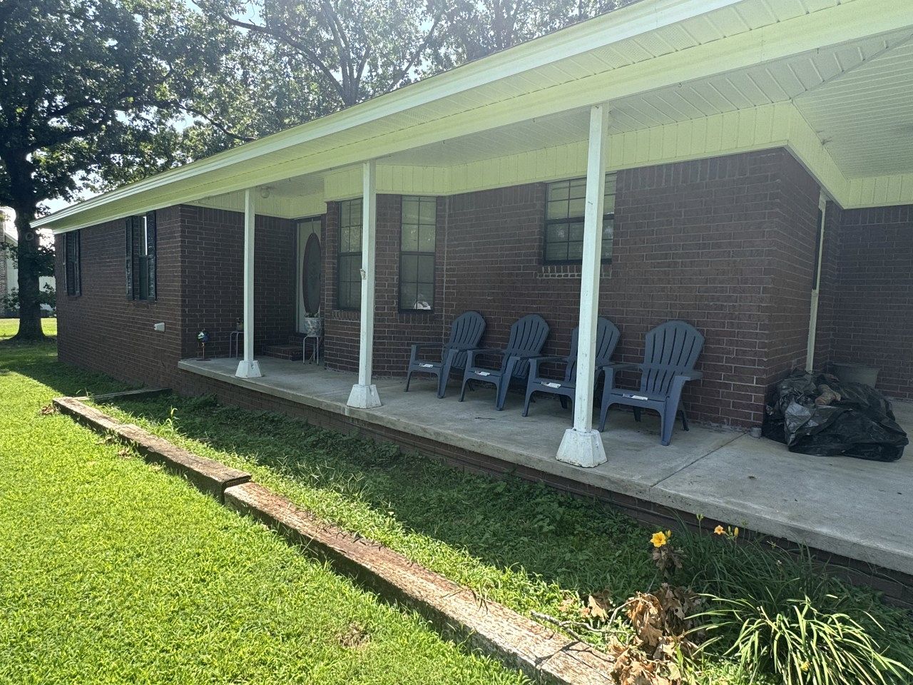 A building with a covered porch, brick walls, and several plastic chairs.
