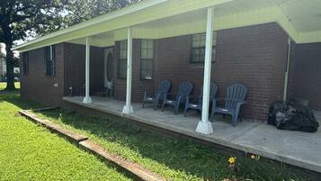 A building with a covered porch, brick walls, and several plastic chairs.