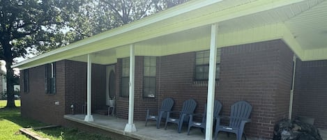 A building with a covered porch, brick walls, and several plastic chairs.