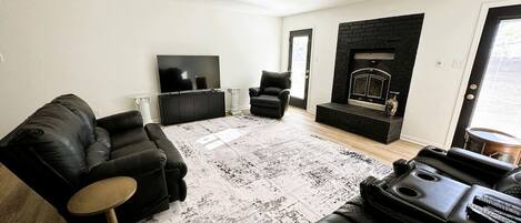 A modern living room with a black leather sofa, a black leather armchair, a small round table, a fireplace, and a ceiling fan.