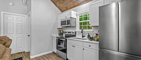 A modern kitchen with white cabinets, stainless steel appliances, and a wooden ceiling.