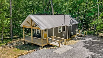A small cabin with a porch, a covered seating area, and a gravel driveway.