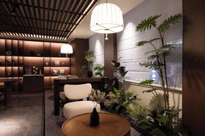 Un interior moderno con zona de comedor, una mesa redonda de madera con un florero y diversas plantas.