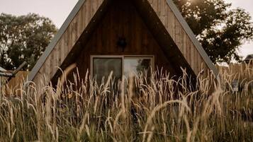 A wooden cabin with a triangular roof, surrounded by tall grass.