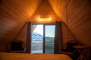 Een gezellige kamer met een bed, twee rieten stoelen, een tafeltje en uitzicht op een besneeuwde berg door een glazen deur.