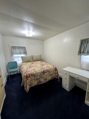 A small, single-room bedroom with a bed, a desk, a chair, and a window with curtains. - Spacious Cottage for a Group Getaway with Views of Harvey Lake in Northwood, New Hampshire (Northwood)