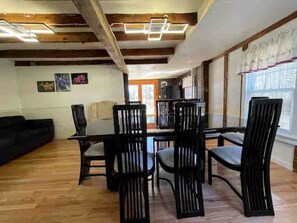A dining area with a wooden table and chairs, a black sofa, and a window with blinds. - Spacious Cottage for a Group Getaway with Views of Harvey Lake in Northwood, New Hampshire (Northwood)