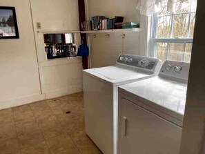 A laundry room with a washing machine and dryer, a shelf with books, and a window with a view of trees. - Spacious Cottage for a Group Getaway with Views of Harvey Lake in Northwood, New Hampshire (Northwood)
