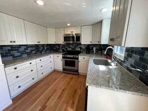 A kitchen with white cabinets, a stainless steel oven, and a granite countertop. - Spacious Cottage for a Group Getaway with Views of Harvey Lake in Northwood, New Hampshire (Northwood)