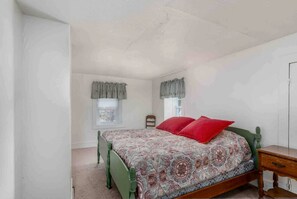 A bedroom with a bed, a nightstand, a chair, and a window with curtains. - Spacious Cottage for a Group Getaway with Views of Harvey Lake in Northwood, New Hampshire (Northwood)