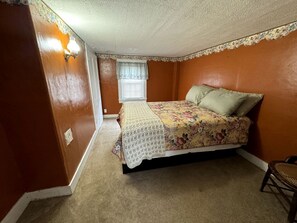 A bedroom with a bed, a window, a wall-mounted light, and a door. - Spacious Cottage for a Group Getaway with Views of Harvey Lake in Northwood, New Hampshire (Northwood)