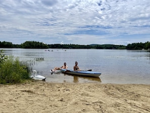 Ein sandiger Strand mit einem ruhigen See, einem kleinen Boot und zwei Personen, die im Boot sitzen.