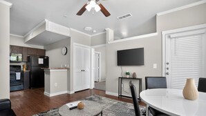 Una cocina moderna con refrigerador, microondas y horno. Hay un comedor con mesa y sillas, una alfombra pequeña y un ventilador de techo.
