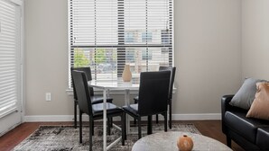 Un comedor con una mesa y sillas, una ventana con persianas, un jarrón y un sofá con cojines.