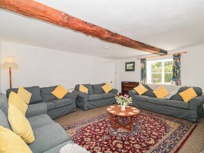 A living room with grey sofas, yellow cushions, a round wooden coffee table, and a patterned rug. - Walk Farmhouse (Gloucester)