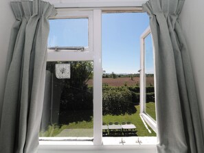 A window with curtains, a view of a green landscape, and a white building in the distance. - Walk Farmhouse (Gloucester)