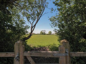A wooden gate leading to a green field with trees in the background. - Walk Farmhouse (Gloucester)