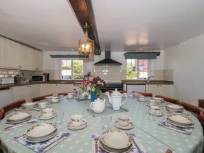 A dining room with a table set for a meal, kitchen area with appliances, and a view of the outdoors. - Walk Farmhouse (Gloucester)