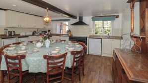 A kitchen with a dining table set for six, wooden chairs, a hanging light fixture, and a view of the outdoors through a window. - Walk Farmhouse (Gloucester)