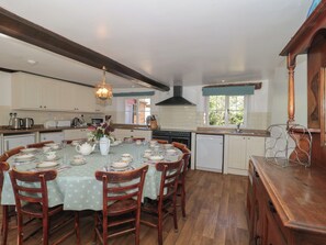 A kitchen with a dining table set for six, wooden chairs, a hanging light fixture, and a view of the outdoors through a window. - Walk Farmhouse (Gloucester)