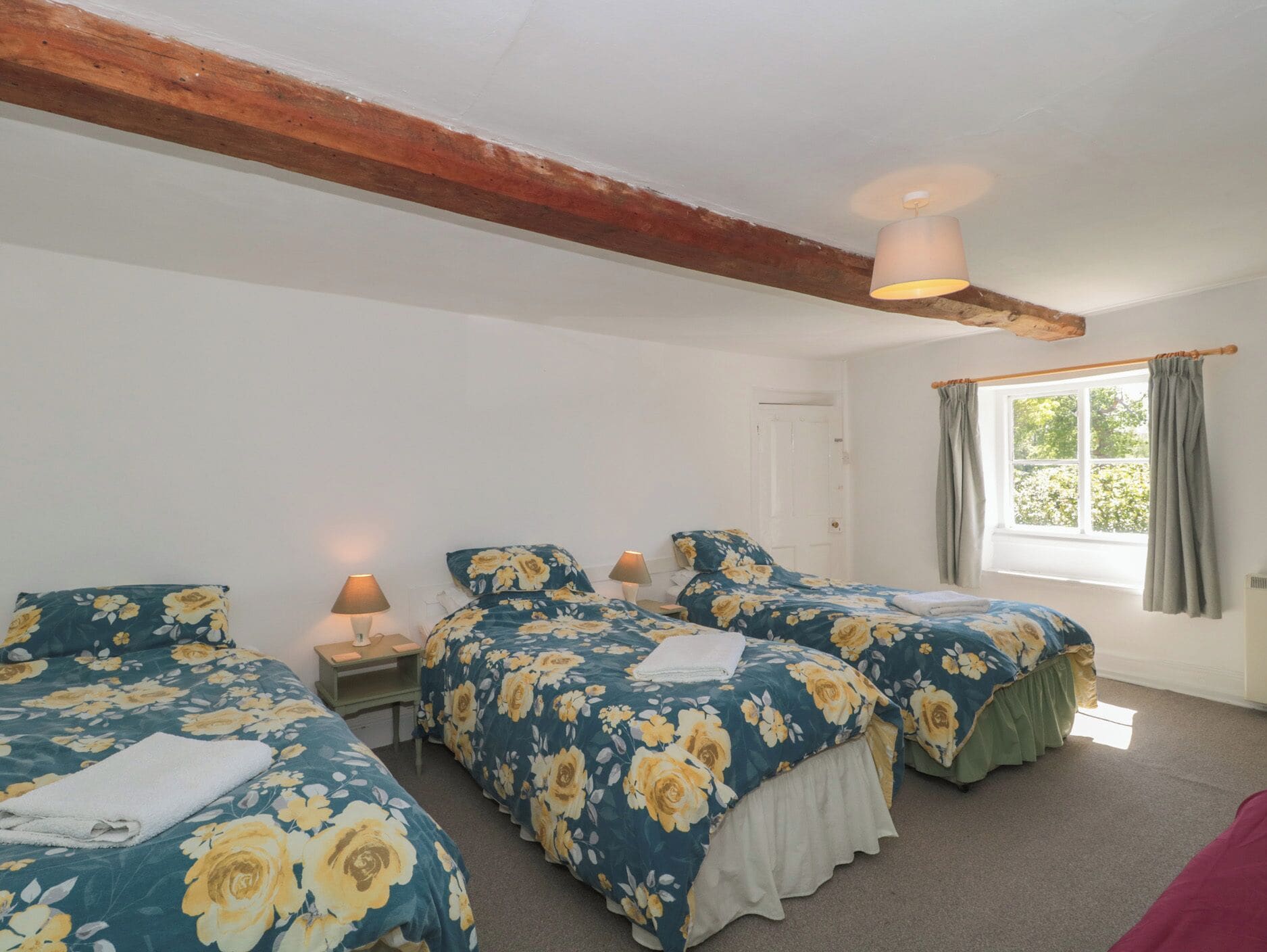 Quarto com duas camas, janela com cortinas, vigas de madeira no teto e abajur.