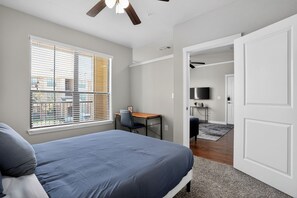 Un dormitorio con cama, escritorio, silla, televisor y puerta que da a otra habitación.