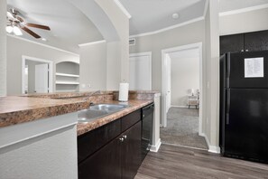 Eine moderne Küche mit Granit Arbeitsplatten, dunklen Schränken, einem schwarzen Kühlschrank und einem Deckenventilator.