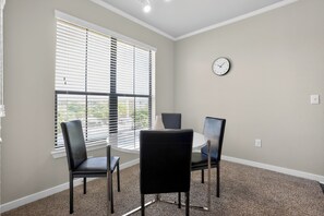 A room with a round table, two chairs, a clock on the wall, and a window with blinds. - Cozy 2BR with modern finishes (New Braunfels)