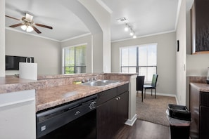 A modern kitchen with granite countertops, a dishwasher, and a ceiling fan. - Cozy 2BR with modern finishes (New Braunfels)