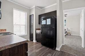 A modern kitchen with a black refrigerator, wooden cabinets, and a granite countertop. - Cozy 2BR with modern finishes (New Braunfels)