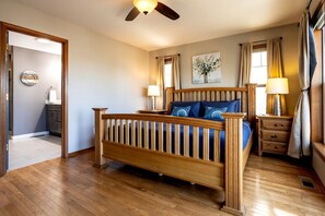 Ein Schlafzimmer mit einem hölzernen Bett, Deckenventilator, Nachttisch und einem fenster mit Vorhängen.