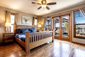 A bedroom with a wooden bed, two bedside tables, a ceiling fan, and a large window with a view. - Relaxing Coastal Getaway with Bay Views in Blaine, Washington (Blaine)