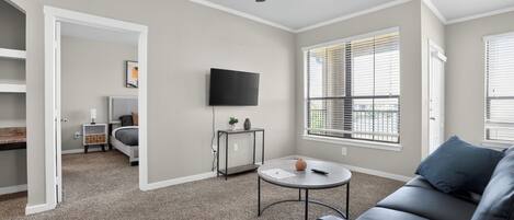 Un salon équipé d’un ventilateur de plafond, d’un téléviseur, d’un canapé, d’une table basse et d’une fenêtre avec des stores.