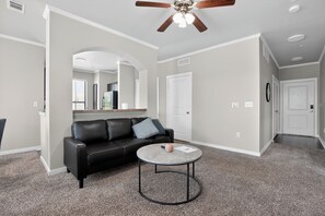 Ein Wohnzimmer mit einer schwarzen Ledersofa, einem runden Couchtisch, einem Deckenventilator und einer Tür.