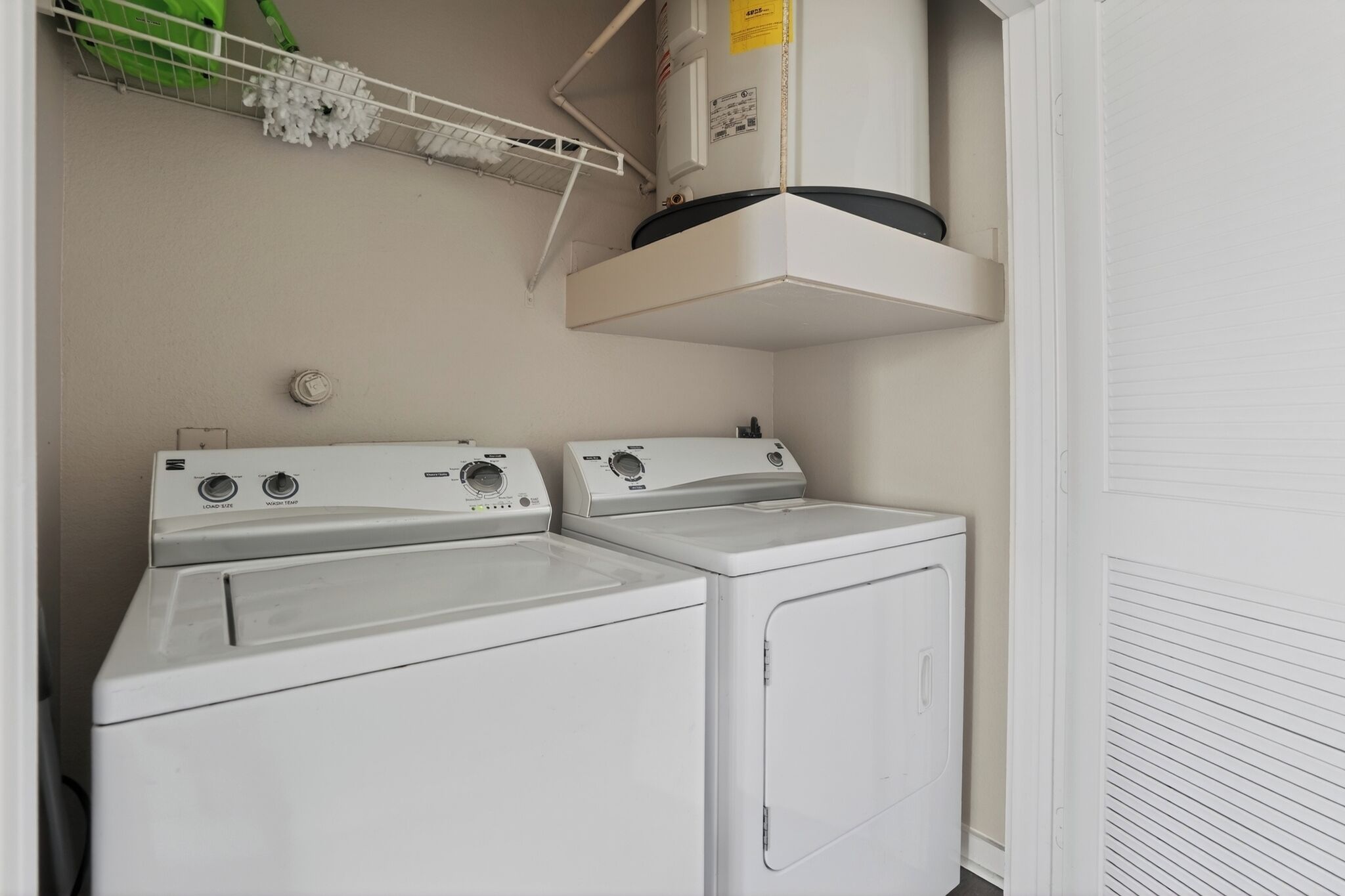 A laundry area with two washing machines and a dryer, a shelf with cleaning supplies, and a white door.
