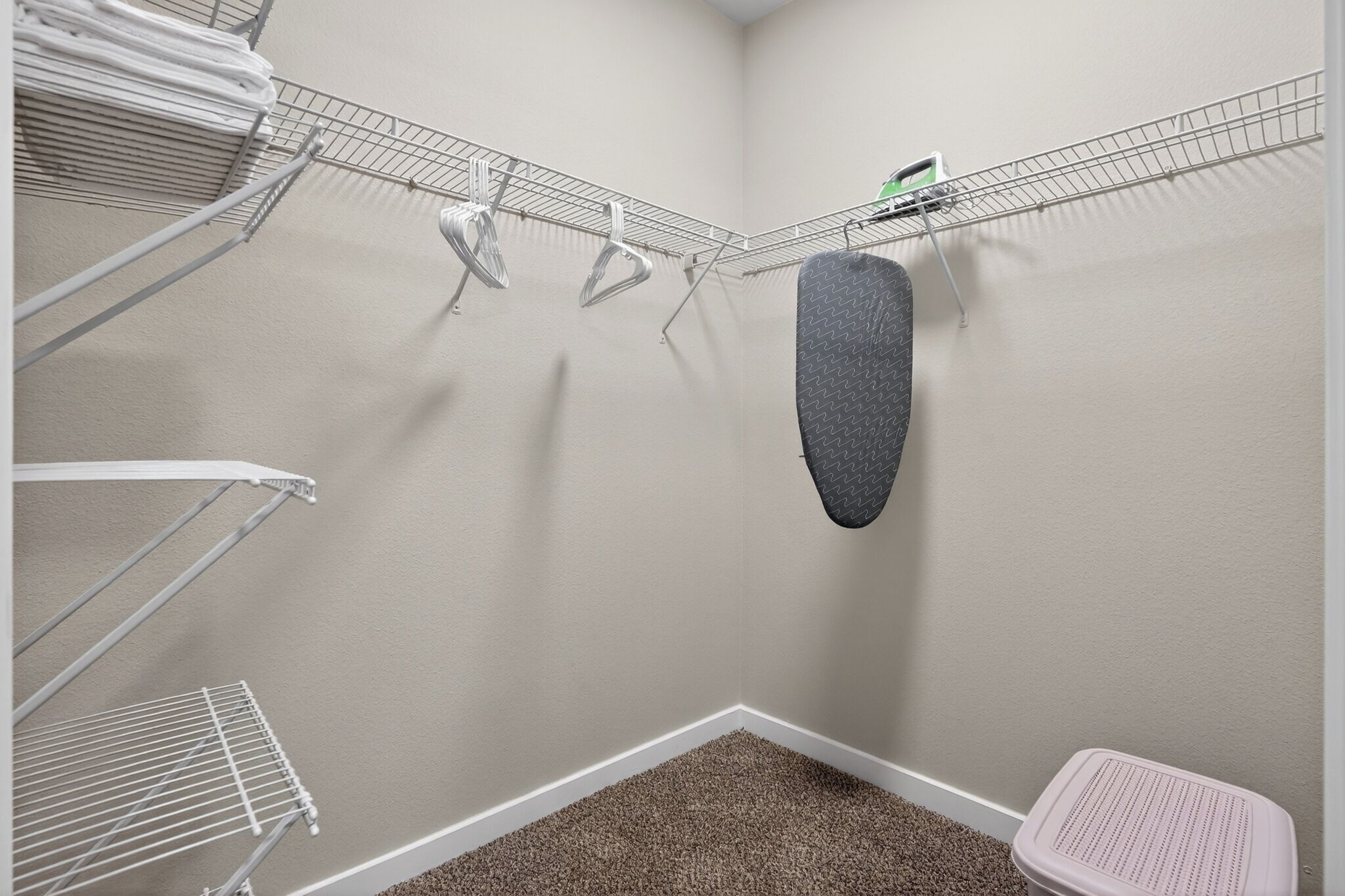 A laundry area with metal drying racks, a hanging mat, and a small stool.