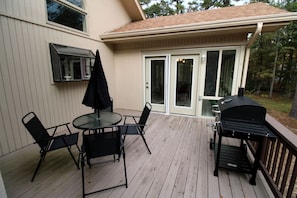 Een terras met een glazen tafel en stoelen, een barbecue en een schuifpui die leidt naar een overdekt terras.