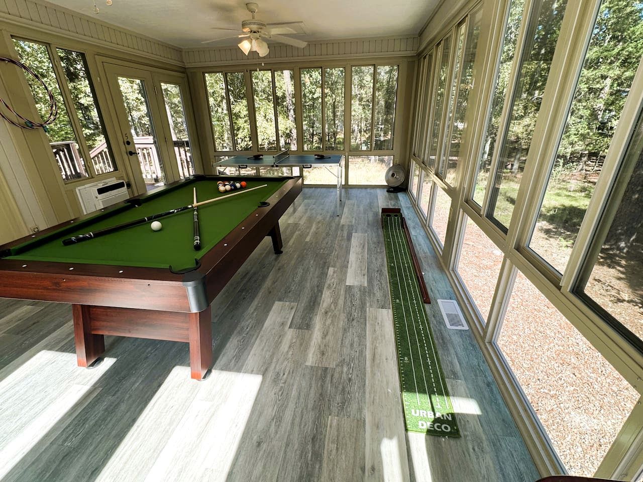 A pool table in a room with large windows and a view of trees.