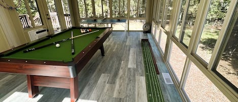 Una mesa de billar en una sala con ventanas amplias y vistas a árboles.