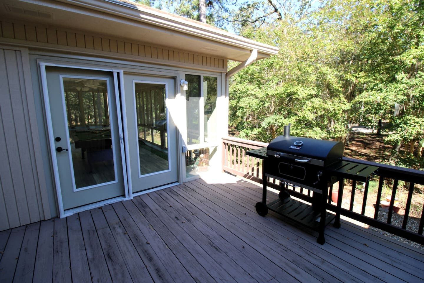 A covered deck with a barbecue grill, sliding glass doors, and a wooden railing.