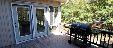 Une terrasse couverte équipée d’un barbecue, de portes-fenêtres coulissantes et d’une rambarde en bois.