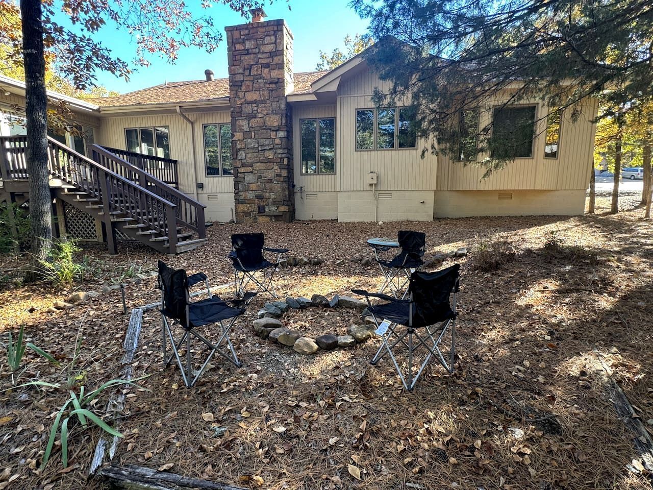 A house with a stone fireplace, outdoor seating, and a staircase leading to a deck.