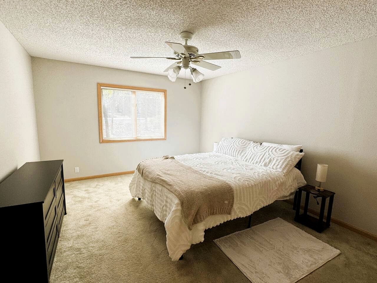 A bedroom with a bed, a ceiling fan, a window, a dresser, and a nightstand.